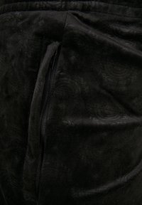 Sort velourstof med et subtilt præget mønster. Har en sidelomme med lynlås, glat tekstur og elastisk taljebånd.