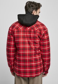 Rød- og svart rutete skjorte med svart hette, med lange ermer og knappeender, laget av et vevd, teksturert stoff.