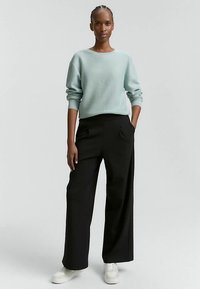 Gaiši zils fakturēts džemperis ar garām piedurknēm, kombinēts ar augsta vidukļa melnām biksēm un baltiem sporta apaviem. Vienkāršs, relaksēts piegriezums.