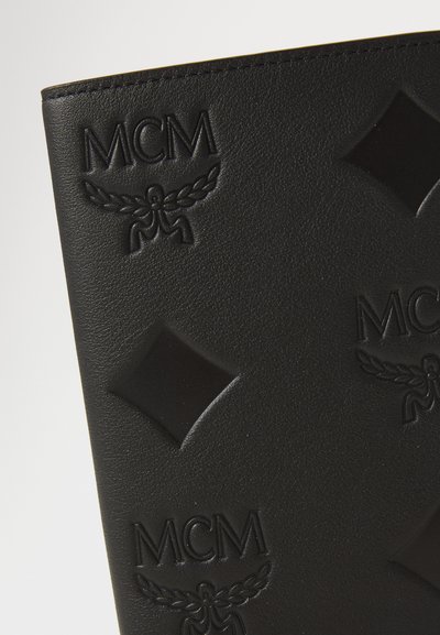 Obiect din piele neagră cu logo-ul MCM embosat și modele în formă de diamant. Suprafață texturată cu detalii ridicate și accente netede.