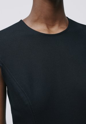 Zbliżenie osoby noszącej czarny bezrękawnik z widocznymi detalami szwów w okolicy ramienia i klatki piersiowej.