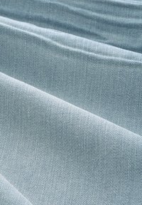 Tissu en denim bleu clair plié en crêtes parallèles et douces, montrant une texture détaillée et un motif de tissage.