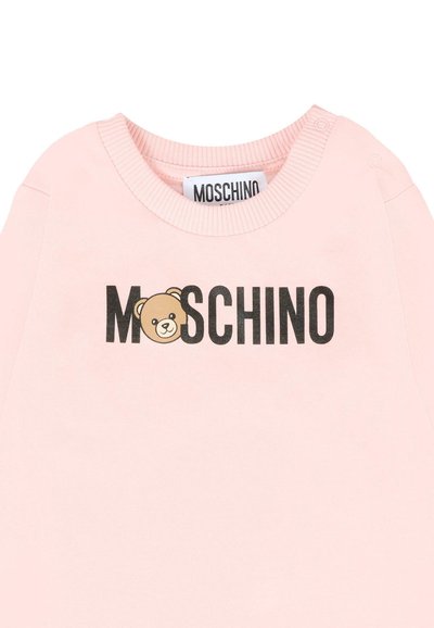 Felpa di cotone rosa con scollo rotondo e bottoni a pressione. La parte frontale presenta il logo "Moschino" e un'illustrazione di un orso in nero e beige.