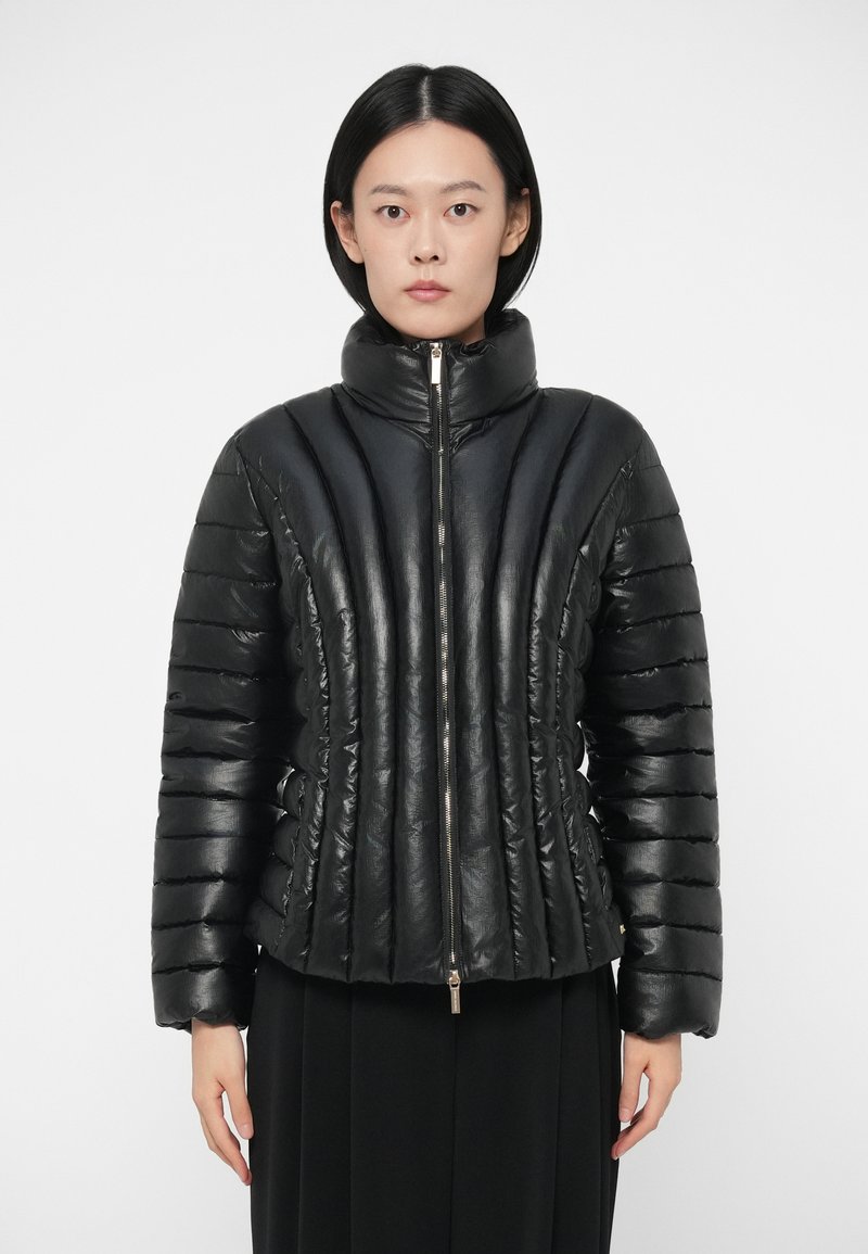 Svart polstret jakke med høy krage, glidelås og vertikal stripet tekstur. Laget av blankt materiale, med en tettsittende design.