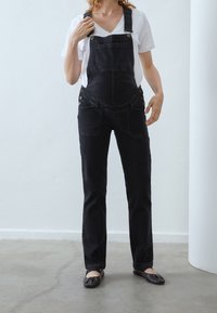 Svarta jeansoverall med figursydd midja, justerbara axelremmar och två framfickor. Kombinerat med en vit V-hals t-shirt och platta skor.