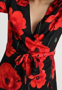Černé zavinovací  šaty s velkými červenými máky, hlubokým výstřihem do V a detailem na zavazování v pase. Hladká látka s zelenými akcenty na okvětních lístcích.