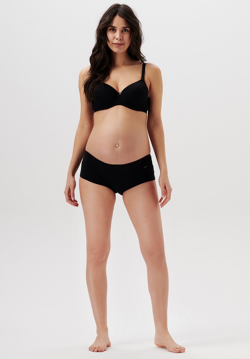 Svart graviditetstopp med sömlösa kupor och justerbara axelremmar, parat med matchande svarta hipster-shorts. Tyget ser mjukt och elastiskt ut.