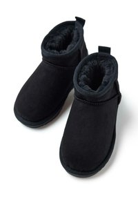 Botines de ante negros con un suave forro de piel, punta redondeada y una pestaña para facilitar su colocación. Detalles de costura a lo largo de los lados.