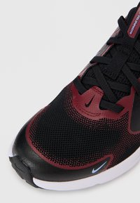 Black and burgundy athletic shoe, featuring mesh upper, textured accents, and white sole. Eye-catching Nike logo on the side.