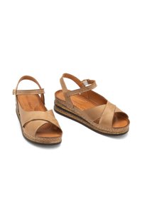 Brązowe skórzane sandały z krzyżowym paskiem, otwartym noskiem i regulowanym paskiem na pięcie. Korkowa podeszwa na koturnie zwiększa wysokość i komfort.