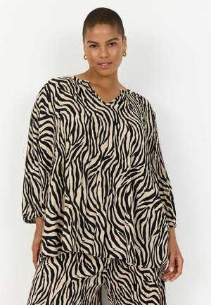 Blusa beige con strisce zebra nere, scollatura a V e maniche lunghe. Tessuto morbido con una vestibilità ampia, abbinata a pantaloni con lo stesso motivo.
