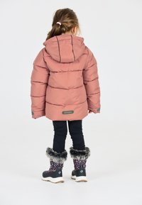 Lyserød pufferjakke med hætte, der har et quiltet design og grå accenter. Båret over sorte bukser og blomsterstøvler med pelskant.