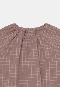 Fialový látkový top s nařaseným výstřihem, zdobený světle růžovým mřížkovaným vzorem. Textura je hladká a elastická, navržená s důrazem na pohodlí.