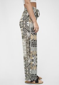 Trykte vide bukser med en blanding av svarte, hvite og gullmønstre, med snøring i midjen og avslappet passform. Strukturert stoff.