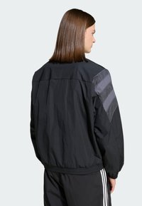 Čierna vetrovka s mierne lesklým povrchom, elastickými manžetami a sivými horizontálnymi pruhmi na ramenách.