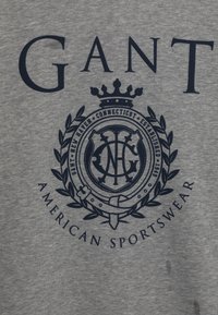 Tessuto grigio con logo GANT blu navy, un emblema coronato e testo "New Haven Connecticut Established 1949 American Sportswear."