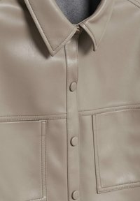 Beige lederen shirt met een klassieke kraag, voorzien van een knoopsluiting aan de voorkant, twee borstzakken en een gladde textuur.