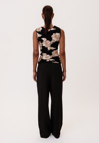 Fekete virágmintás ujjatlan blúz arany díszítéssel, laza fekete nadrággal párosítva. Az anyag lágy és sima tapintású.