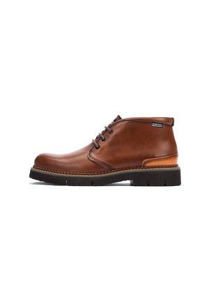 Bottes en cuir marron à la cheville avec une finition lisse, un accent talon contrastant, une pointe ronde et un système de laçage. Semelle en caoutchouc épais avec un motif de crampons.