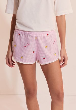 Pantalones cortos de cuadros vichy rosa con patrones de frutas bordadas y borde de encaje blanco, llevados por una persona con una camiseta blanca de manga corta.
