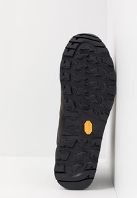 Schwarze Gummisohle mit tiefen Profilen, mit einem gelben Vibram-Logo; Obermaterial aus dunklem, strukturiertem Material, das Haltbarkeit und Traktion zeigt.