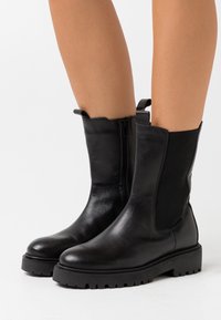 Botas de cuero negro hasta el tobillo con paneles laterales elásticos, una lengüeta para facilitar el calzado y una suela de goma resistente con un dibujo profundo para mayor tracción.