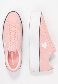 Baskets basses en daim rose avec une étoile blanche en accent, semelle en caoutchouc blanche plate et design classique à lacets avec détails perforés.