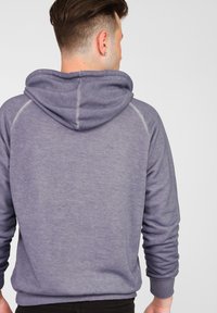 Grå sweatshirt med huva, som har en mjuk textur och ribbade muddar. Designen inkluderar kontrasterande sömmar på baksidan.