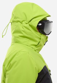 Veste imperméable vert vif avec capuche réglable et col haut, dotée d'accents noirs, d'une texture lisse et de lunettes de ski.