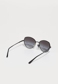 Óculos de sol pretos em forma de gato com armação de metal, lentes cinzentas Graduadas e hastes finas com uma marcação subtil. Inclui almofadas nasais ajustáveis.