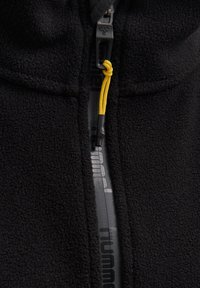 Chaqueta de forro polar negra con un destacado cierre frontal con un cordón amarillo y un logo en la tela, que resalta la suave textura y el calor.