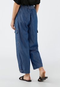 Pantalones cargo de mezclilla azul con un corte relajado, cintura elástica, puños ajustados y bolsillos laterales. Diseño sencillo y textura suave.