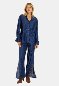Conjunto de pijama azul marino con un patrón texturizado, que incluye una camisa con botones y pantalones acampanados con aberturas laterales. Tela suave y sedosa.