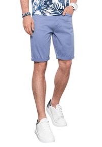 Pantaloni corti di cotone lilla con orli arrotolati; abbinati a sneaker bianche con dettagli neri. L'outfit include una camicia con fantasia floreale.
