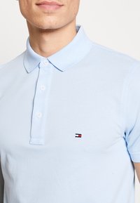 Ljusblå pikétröja i bomull med klassisk krage, treknappars knäppning och en liten logotyp på vänster bröst.