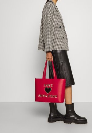 Czerwona torba na ramię z nadrukiem "LOVE" i złotym sercem, zestawiona z czarno-białą kratowaną marynarką, czarną skórzaną spódnicą i masywnymi czarnymi butami.