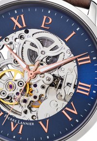 Montre squelette avec un cadran bleu, un boîtier en métal argenté et des chiffres romains en or rose. Le mouvement exposé révèle des engrenages et des accents en or et en violet.