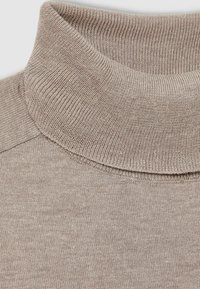 Pull beige en maille avec col roulé tricoté montrant un col côtelé détaillé et une texture de corps lisse en tricot.