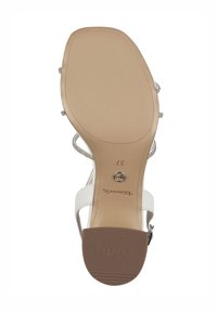 Weiße Sandalen mit einer glatten, strukturierten Sohle. Verfügen über schlanke Riemen und Metallbeschläge. Die Sohle hat ein hellbraunes Gummi-Finish.