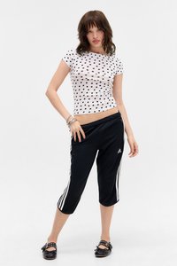 Hvit t-skjorte med prikkete mønster og en tettsittende design, kombinert med svarte avkuttede bukser med hvite side-striper og et Adidas-logo. Flate sorte sko.