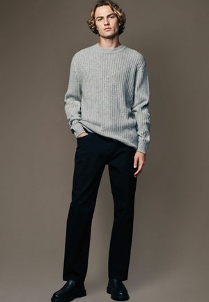 Grau gerippter Strickpullover, schwarze gerade geschnittene Hose und schwarze Schuhe. Schlichtes Design, lockere Passform und strukturierte Stoffdetails.