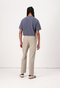 Blauw katoenen T-shirt met korte mouwen, gecombineerd met lichtbeige broek met een elastische tailleband en twee achterzakken. Casual schoeisel zichtbaar.