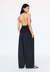 Černý halter top bez zadního dílu spárovaný s kalhotami širokých nohavic. Materiál má hladkou texturu a úbor obsahuje boční kapsy.