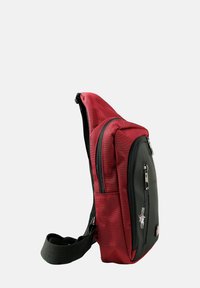 Sac en bandoulière rouge et noir, fabriqué en tissu résistant, avec plusieurs compartiments zippés, une silhouette plate et une bandoulière ajustable.