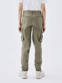 Pantalons cargo en coton vert olive, dotés de deux poches latérales, de poignets élastiques et d'une coupe décontractée. Portés avec des baskets blanches.