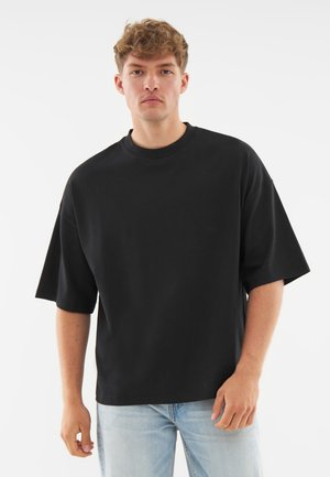 Sort oversized t-shirt lavet af glat stof, med rund hals og kortærmer, iført med lyseblå jeans.
