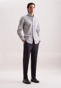 Camicia a scacchi abbottonata in bianco, blu navy e grigio, abbinata a pantaloni sartoriali scuri e scarpe eleganti nere. Tessuto liscio con una vestibilità strutturata.