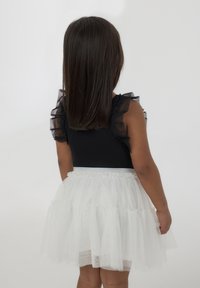 Body nero con maniche corte a volant e gonna in tulle bianco a strati. La gonna presenta una vita argentata e delicate scintille.