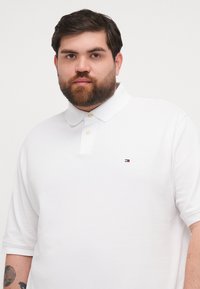 Valge polo särk tekstuurse kangaga, klassikalise krae ja kahe nööbiga. Väike broderieeritud logo vasakul rinnal.