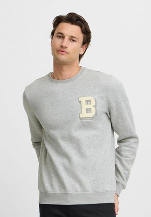 Sudadera gris de tela suave con un escote redondo, mangas largas y una letra "B" en color crema bordada en el lado izquierdo del pecho.
